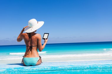 Girl with white hat reads kindle on beach clipart
