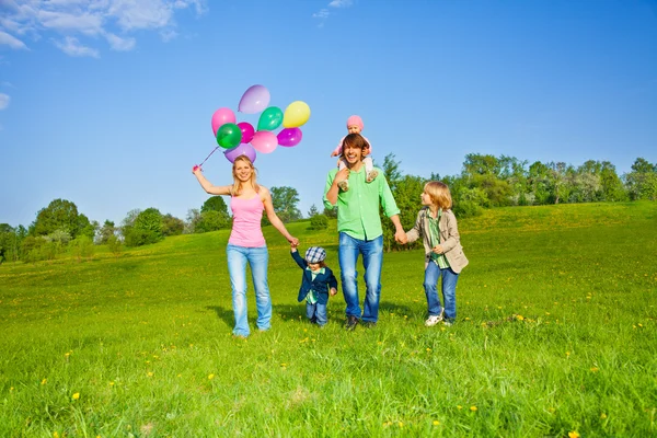 Gelukkige familie wandelingen met ballonnen in park — Stockfoto