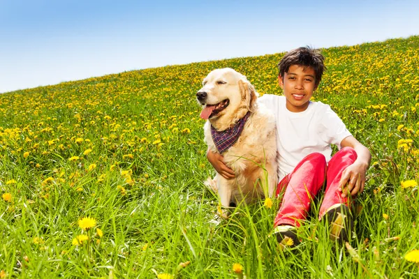 Smiling boy hugs cute dog sitting on green grass