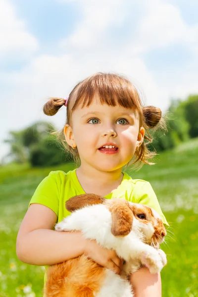 Olhando menina pequena abraçando coelho no campo verde — Fotografia de Stock