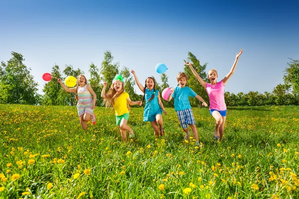 Felice cinque bambini con palloncini corrono in campo — Foto Stock