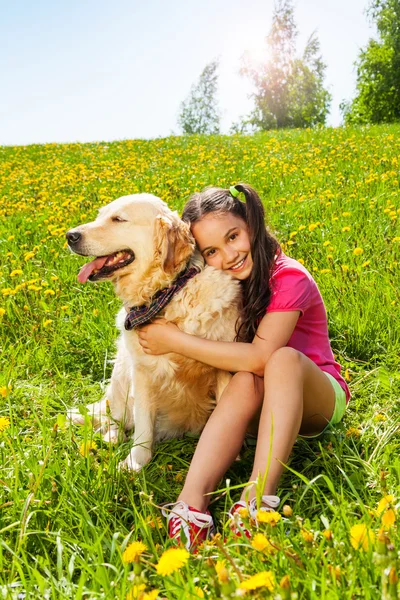 Lächelndes Mädchen umarmt niedlichen Hund, der auf dem Gras sitzt — Stockfoto