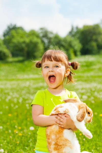 Menina pequena excitada com a boca aberta abraçando coelho — Fotografia de Stock