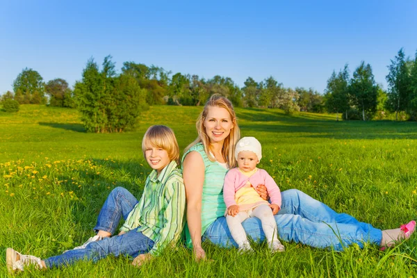 Mère avec des enfants s'assoit sur l'herbe dans le parc — Photo