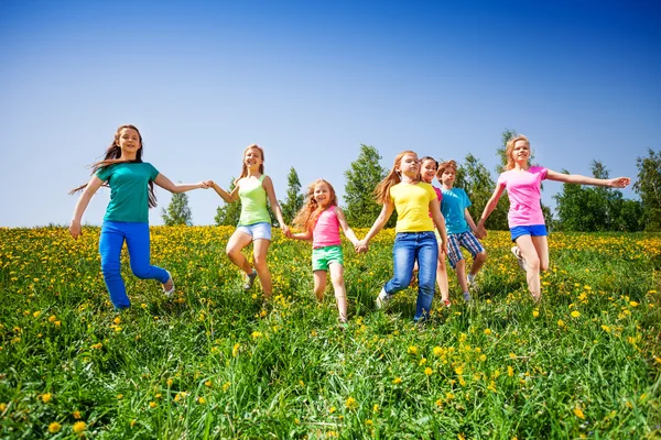 Niños felices corren y se toman de la mano en el prado verde —  Fotos de Stock