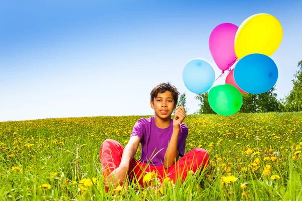 Sitzender Junge mit fliegenden Luftballons im Sommer — Stockfoto