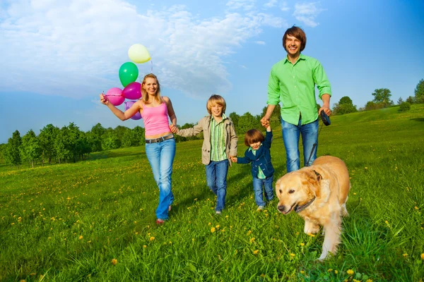 Felici passeggiate in famiglia con palloncini e cane nel parco — Foto Stock