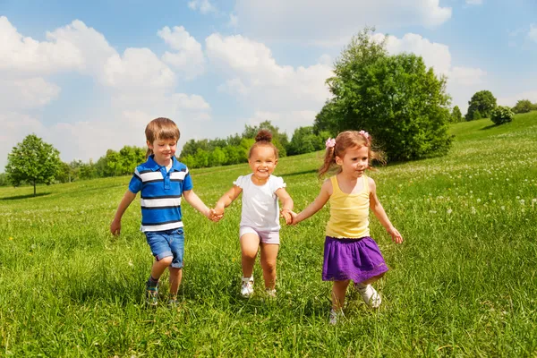 Drei glückliche Kinder, die sich an den Händen halten und spielen — Stockfoto