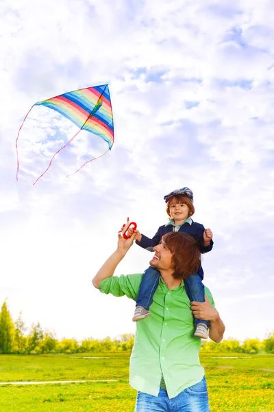 Vater hält Kind mit fliegendem Drachen auf Schultern — Stockfoto