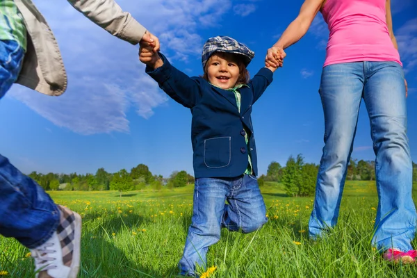 Criança feliz segurando as mãos dos pais no parque — Fotografia de Stock