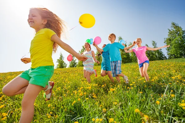 Crianças excitadas com balões correm em campo — Fotografia de Stock