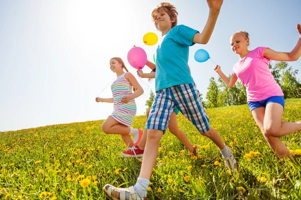 Crianças felizes com balões correm em campo verde — Fotografia de Stock