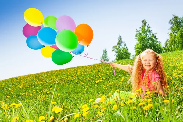 Fröhliches Mädchen mit fliegenden Luftballons sitzt auf Gras — Stockfoto