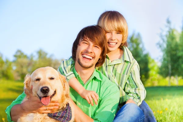 Sorrindo menino, pai e cão sentar no parque na grama — Fotografia de Stock