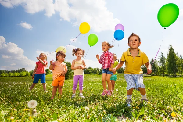 Діти з різнокольоровими повітряними кулями біжать у полі — стокове фото