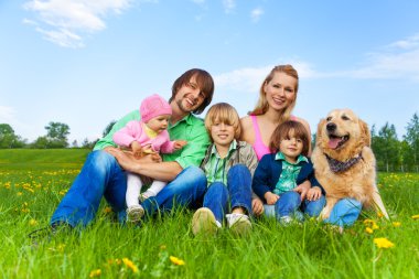 Aile ile köpek yeşil çimenlerin üzerinde oturan gülümsüyor