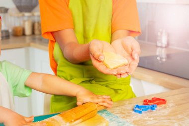 Çocuğun elleri masada pişmeye hazır taze hamurdan yapılmış kalp şeklindeki kurabiyeyi gösteriyor.