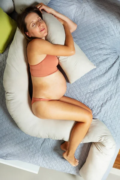 幸せな妊娠中の女性Layオンザベッド抱擁枕のために期待母親ビューから上 — ストック写真