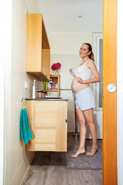 幸せな妊娠中の女性立ちますでザバスルーム近くミラーとシンクタッチ彼女の腹持ち上げシャツ — ストック写真