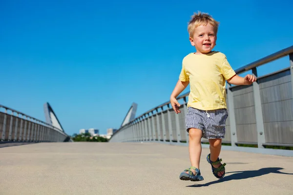 小さなブロンドの幼児男の子ランオンザ歩道橋笑顔 — ストック写真