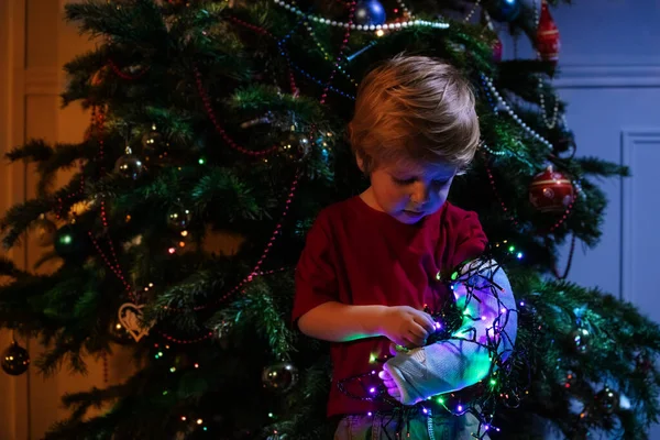 壊れた幼児の少年の手でキャスト照明付きガーランド近くクリスマスツリー — ストック写真