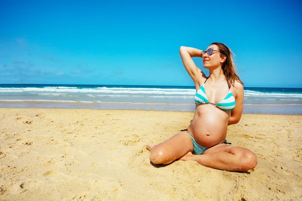 Feliz Mujer Embarazada Relajada Sombrillas Sentarse Playa Tocando Pelo Sonriendo —  Fotos de Stock