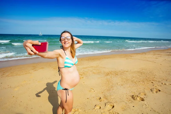 妊娠中の女性オン休暇取ります自殺とともにスマートフォンスタンドオンザ砂の海のビーチ — ストック写真