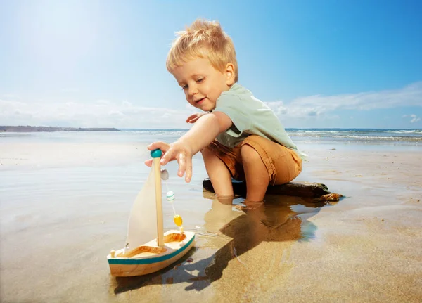 Mały Chłopiec Bawić Się Zabawką Żaglowiec Wodzie Plaży Piasku — Zdjęcie stockowe