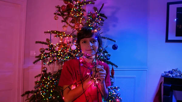 Aydınlatılmış Çelenkli Çocuk Süslenmiş Noel Ağacının Yanında Duruyor — Stok fotoğraf