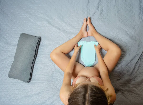 Hamile Kadın Yatağa Oturur Bebek Kıyafetlerini Yukarıdan Görür — Stok fotoğraf