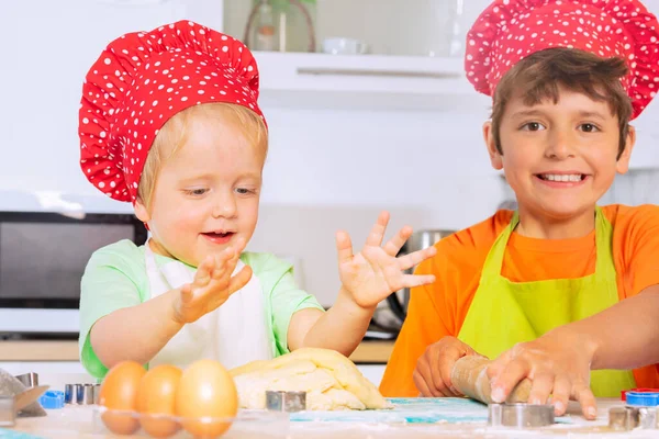 孩子们戴着厨师帽 快乐地微笑着 带着柱塞在厨房桌上滚着面团 — 图库照片