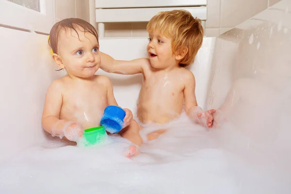 二人の兄弟は泡泡とおもちゃと一緒に家でお風呂で遊ぶ笑顔 — ストック写真