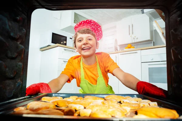 笑顔の男の子はクッキーを取るオーブンから調理帽子とミトンを身に着けている — ストック写真