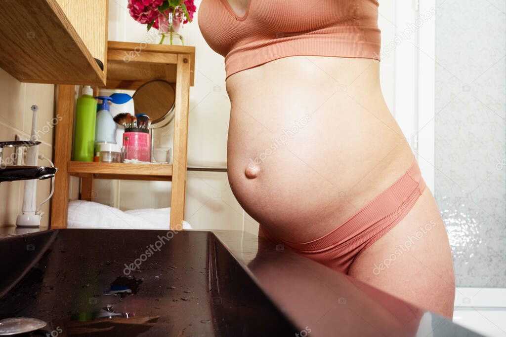 Close-up of a pregnant woman's belly leaning over the sink at the bathroom