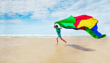 Renkli paraşüt kumaşlı çocuk kumsal dinamik hareket konseptiyle rüzgarda uçuyor.