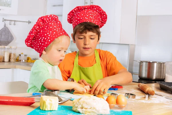 シェフの帽子の小さな子供たちは 家庭のキッチンでクッキーを調理するために生地を焼くと準備する — ストック写真
