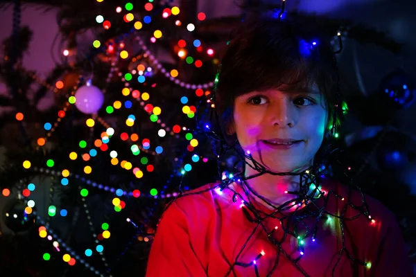 快乐的男孩画像 装饰圣诞树旁点亮的花环灯 淡淡的微笑 — 图库照片