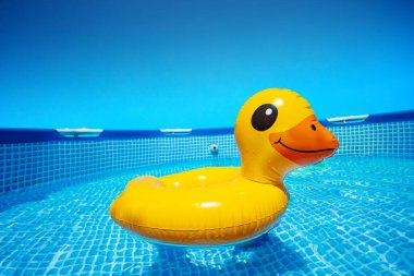 Inflatable cute surprised yellow duck swim in the small summer pool in the garden