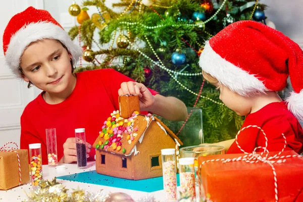 Zwei Kinder Mit Nikolausmütze Kleben Das Lebkuchenhaus Vor Weihnachten Zusammen — Stockfoto