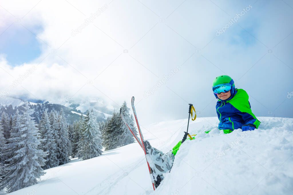 Skier boy sit smiling in the snow over snowy fir forest after heavy snowfall profile view