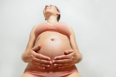 Gülümseyen, mutlu, hamile bir kadın, dilini çıkarıp karnını tutarak yere bakar.