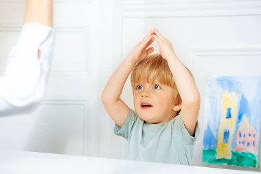 Gelişim aşamasındaki zeki sarışın çocuk sınıfta parmak oyunu oynuyor. Terapist de masanın başında oturuyor.