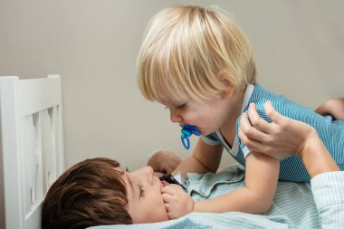 Little blond boy and his brother have fun in the bed playing together