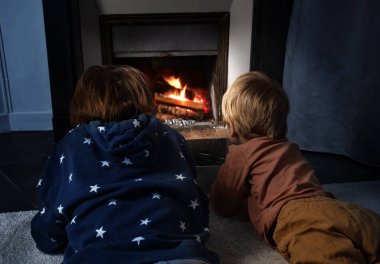 Two boys, brothers lay in front of the home fireplace look at fire