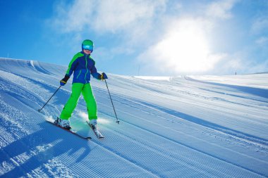 Çocuk yokuş aşağı hızla kayıyor güneşli bir sabahta, güneşli bir günde mavi gökyüzü manzarasında.