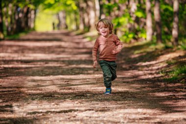 Young little blond boy run on the alley in the park at summer