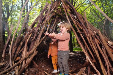 Happy children kids brother and sister girl play with soap bubbles in hut of branches in the forest