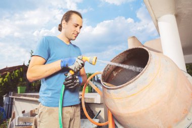 Young man stand cleaning cement mixer at home construction works about to make concrete