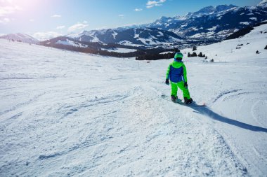 Snowboard yapan çocuğun dağ yamacından aşağı arka görüntüsü.