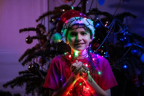 Handen Van Jongen Met Kerstmuts Buurt Van Nieuwjaarsboom Nachts Verlicht — Stockfoto